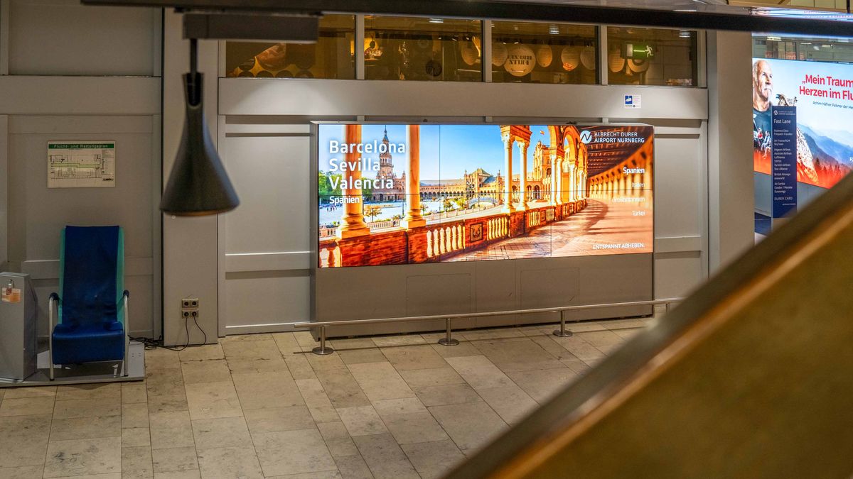 Großflächige Videowand im Flughafenterminal zeigt Spanien-Motiv mit Barcelona, Sevilla und Valencia und dem Claim „Entspannt abheben“