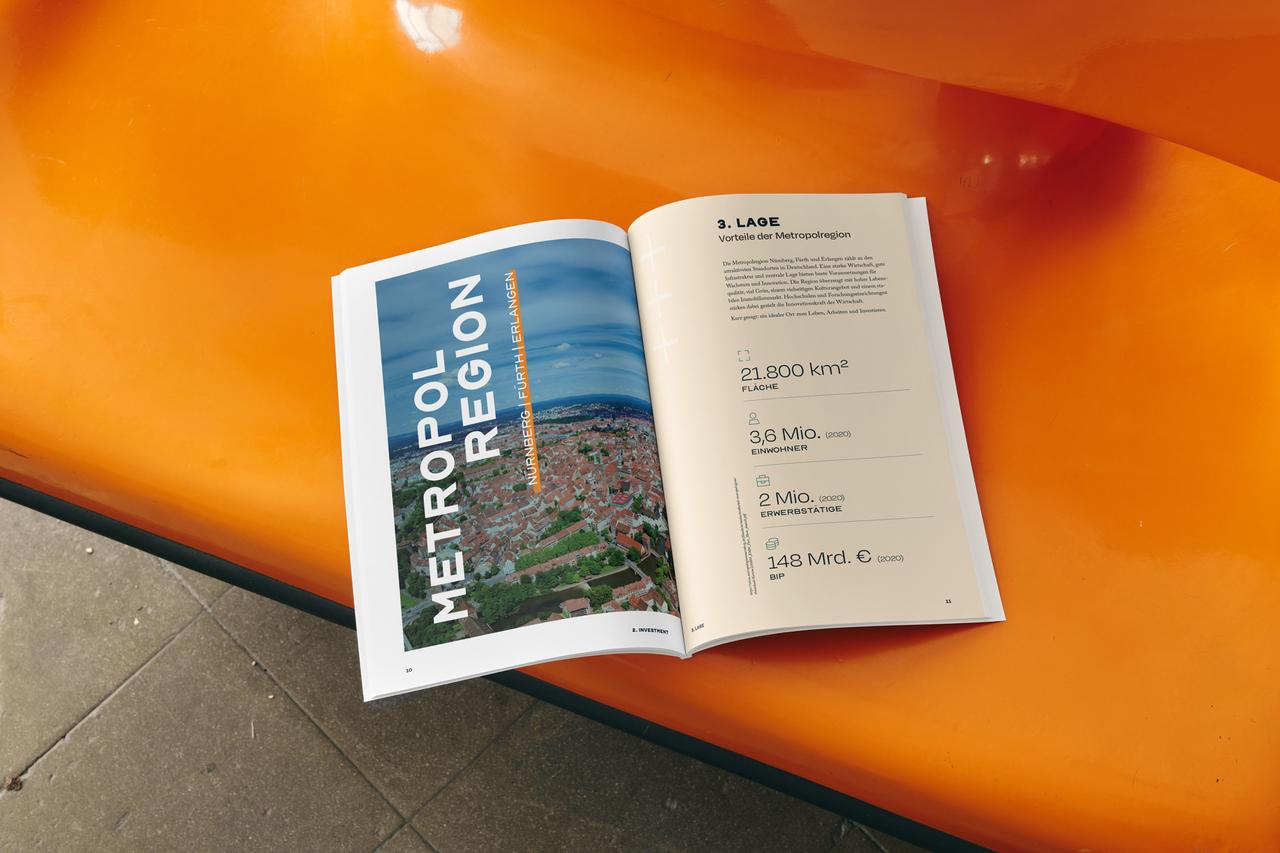 Aufgeschlagenes Central-Homes-Exposé auf orangefarbener Sitzbank, links Luftbild der Metropolregion Nürnberg, rechts Kennzahlen zur Lage