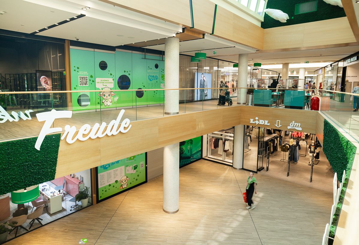 Blick von der Galerie ins FLAiR Fürth: zwei Einkaufsebenen mit grün beklebten Leerflächen, FLAiRY-Motiven und dem Schriftzug „Freude“