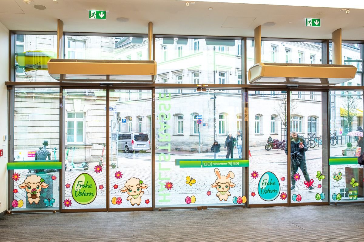 Oster-Beklebung an den Glastüren des Eingangs Hallstraße im FLAiR Fürth: FLAiRY-Schafe, Osterhase, bunte Eier und „Frohe Ostern“