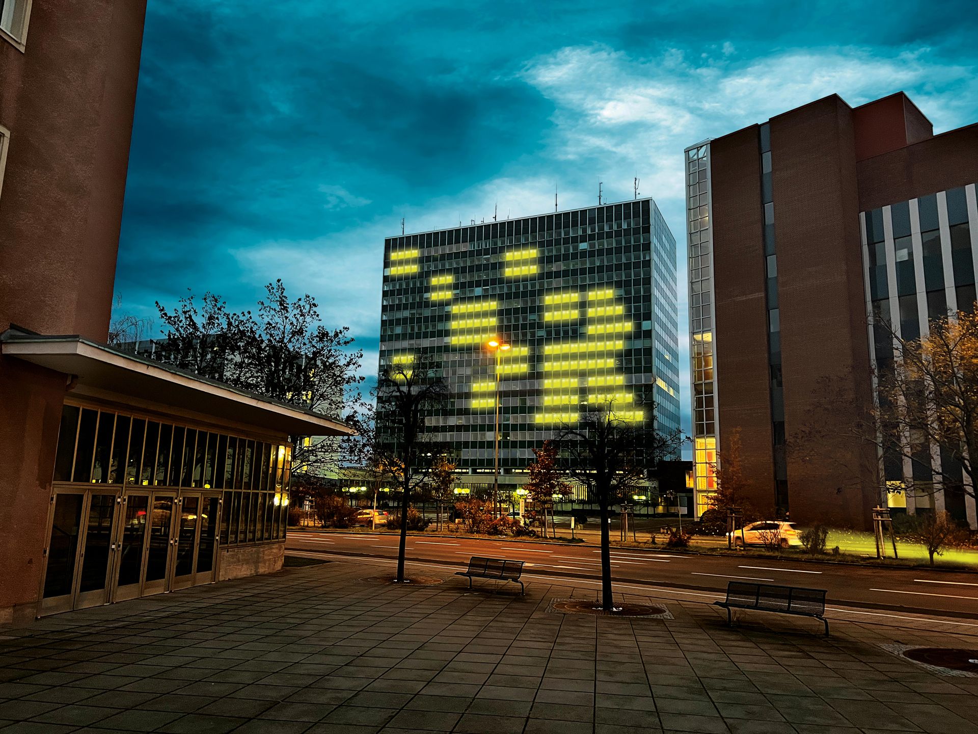 Bürohochhaus in der Abenddämmerung, gelb leuchtende Fenster bilden ein Pixel-Motiv, bearbeitete Aufnahme mit dramatischem Himmel