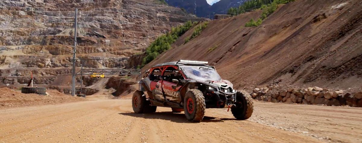 Rot-schwarzer Offroad-Buggy mit Milwaukee-Beklebung fährt über eine staubige Schotterpiste im Tagebau am Erzberg
