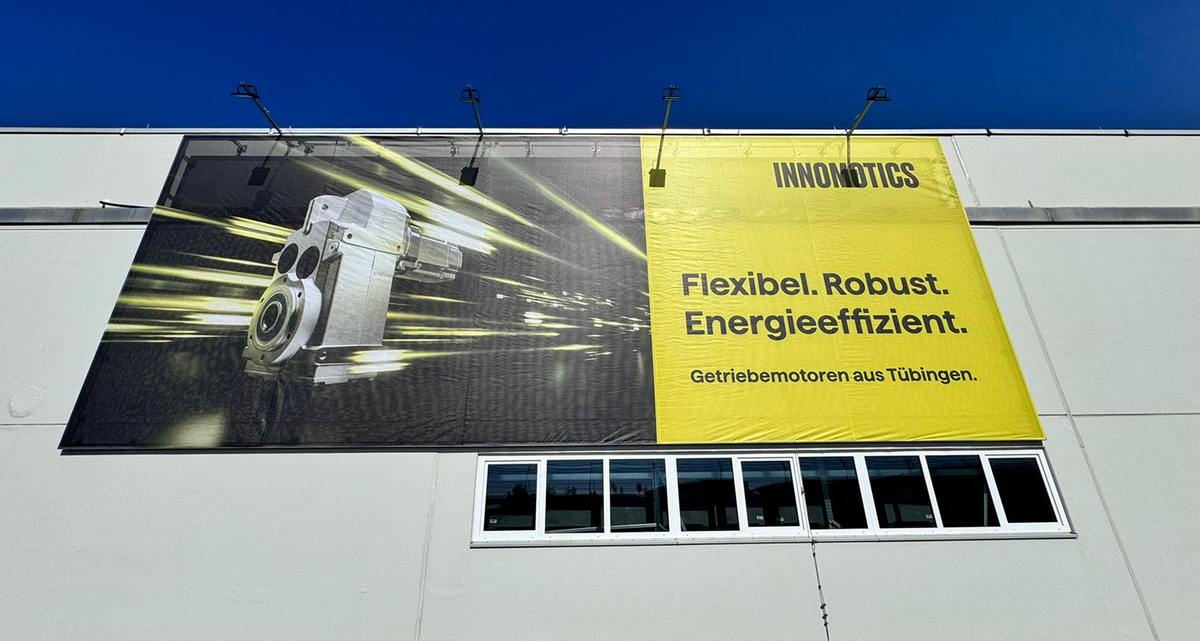 Großflächiges Werbebanner an heller Hallenfassade: links ein Getriebemotor mit Lichtspuren, rechts gelbe Fläche mit „Flexibel. Robust. Energieeffizient. Getriebemotoren aus Tübingen.“