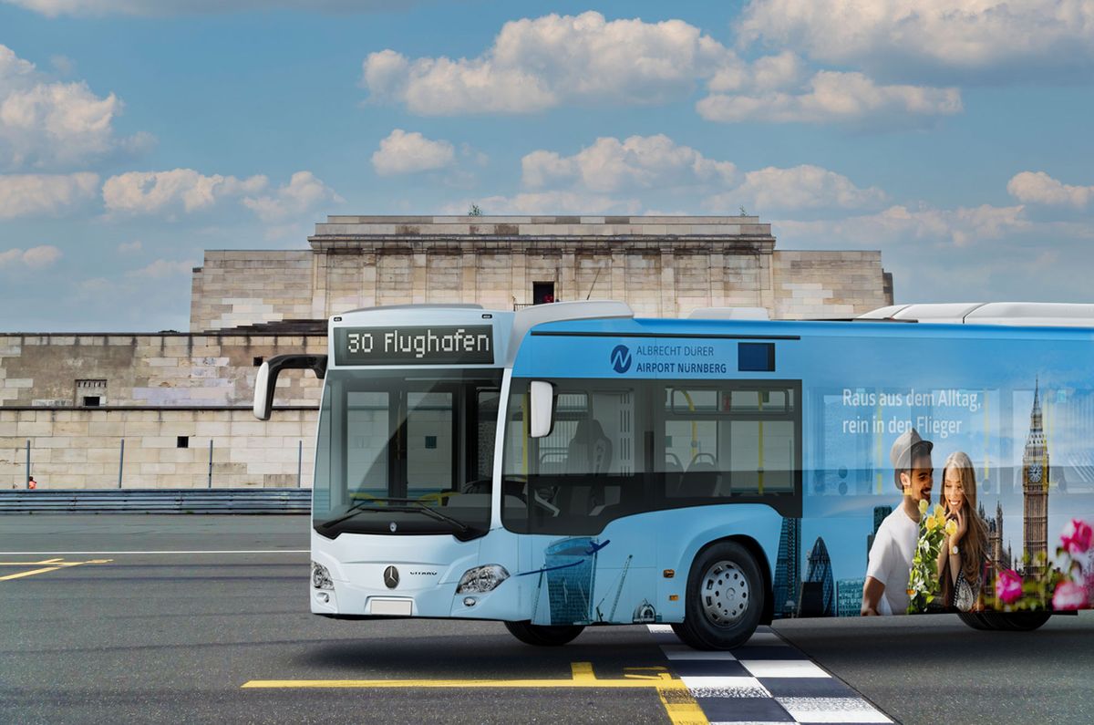 Beklebter Flughafenbus der Linie 30 mit Städtetrip-Motiv auf dem Asphalt vor der Zeppelintribüne in Nürnberg, blauer Himmel mit Wolken