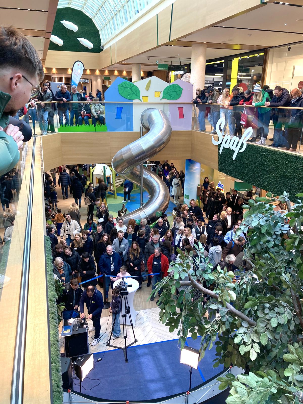 Eröffnung im FLAiR Fürth: dicht gedrängtes Publikum im Atrium vor der Edelstahlrutsche, Zuschauer an den Galerien, vorne eine Bühne mit Kamera und Scheinwerfern