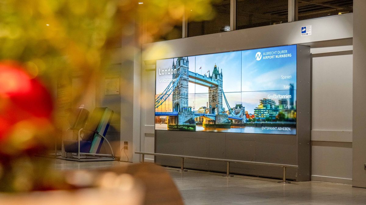 Videowand im Flughafenterminal mit London-Motiv und Tower Bridge, abendliche Aufnahme mit unscharfem Vordergrund