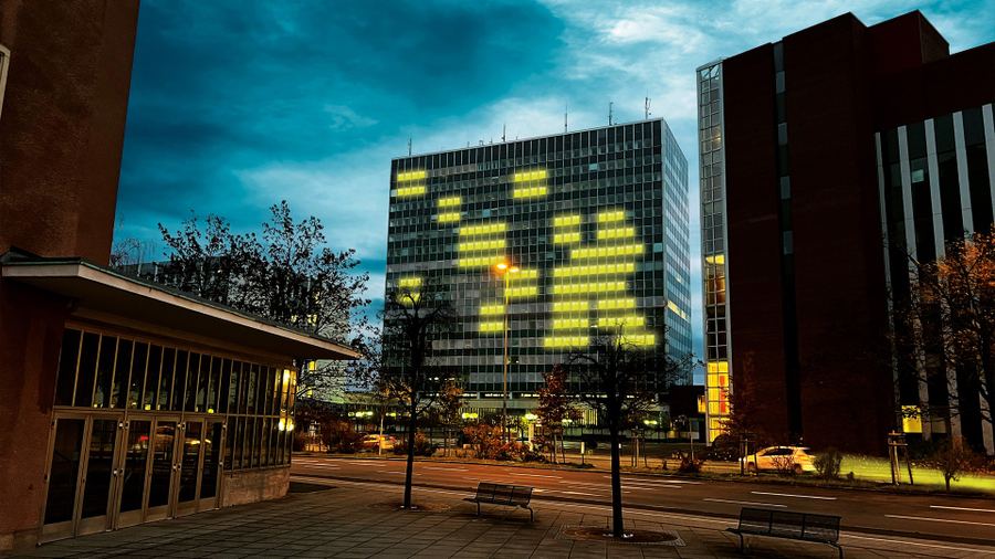 Bürohochhaus in der Dämmerung, dessen beleuchtete Fenster ein gelbes Pixel-Motiv bilden