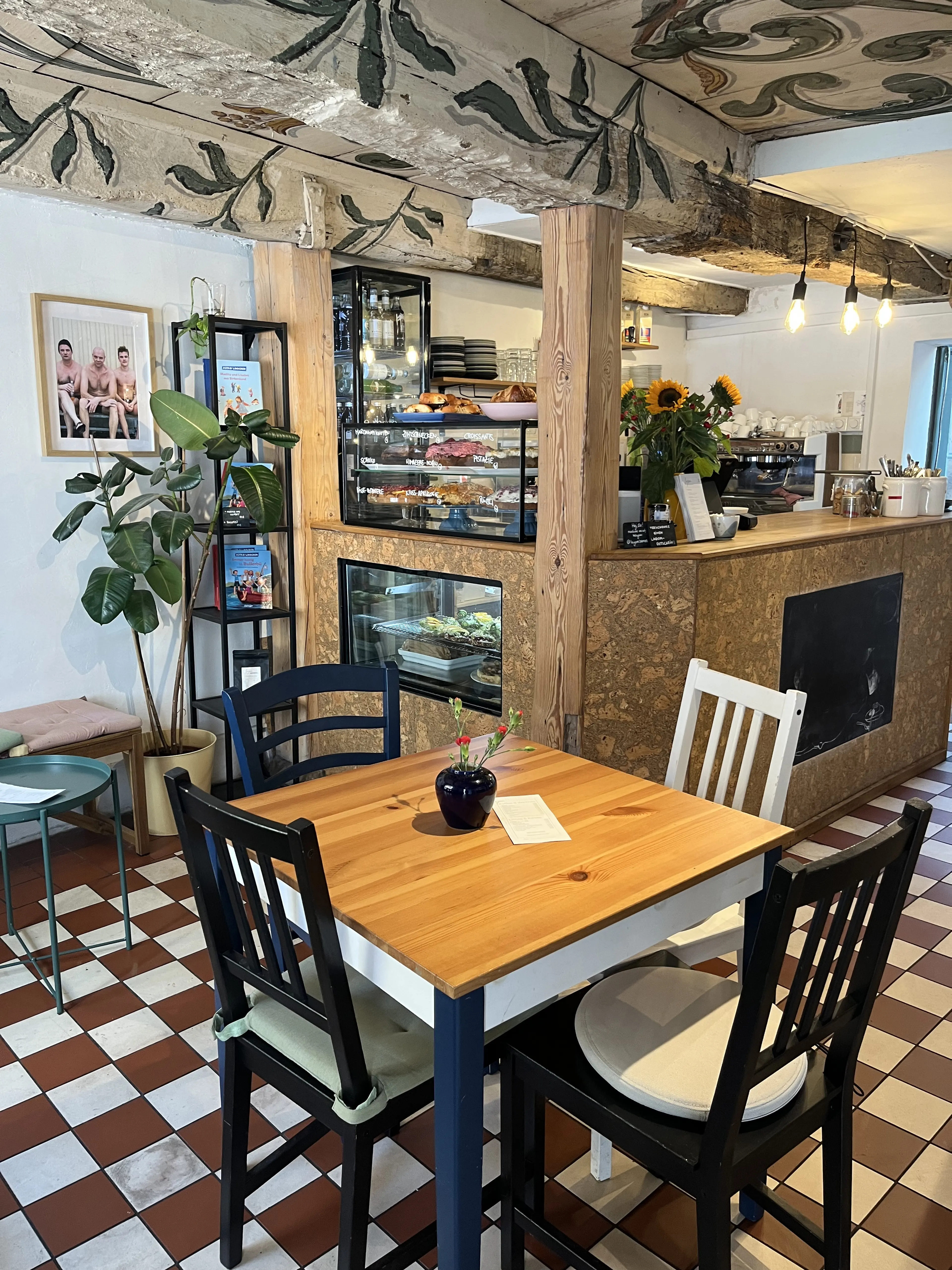 Tresen im Café Lagom mit Siebträger-Espressomaschine, Sonnenblumen und Gebäckvitrine unter der bemalten Deckenbalken-Decke