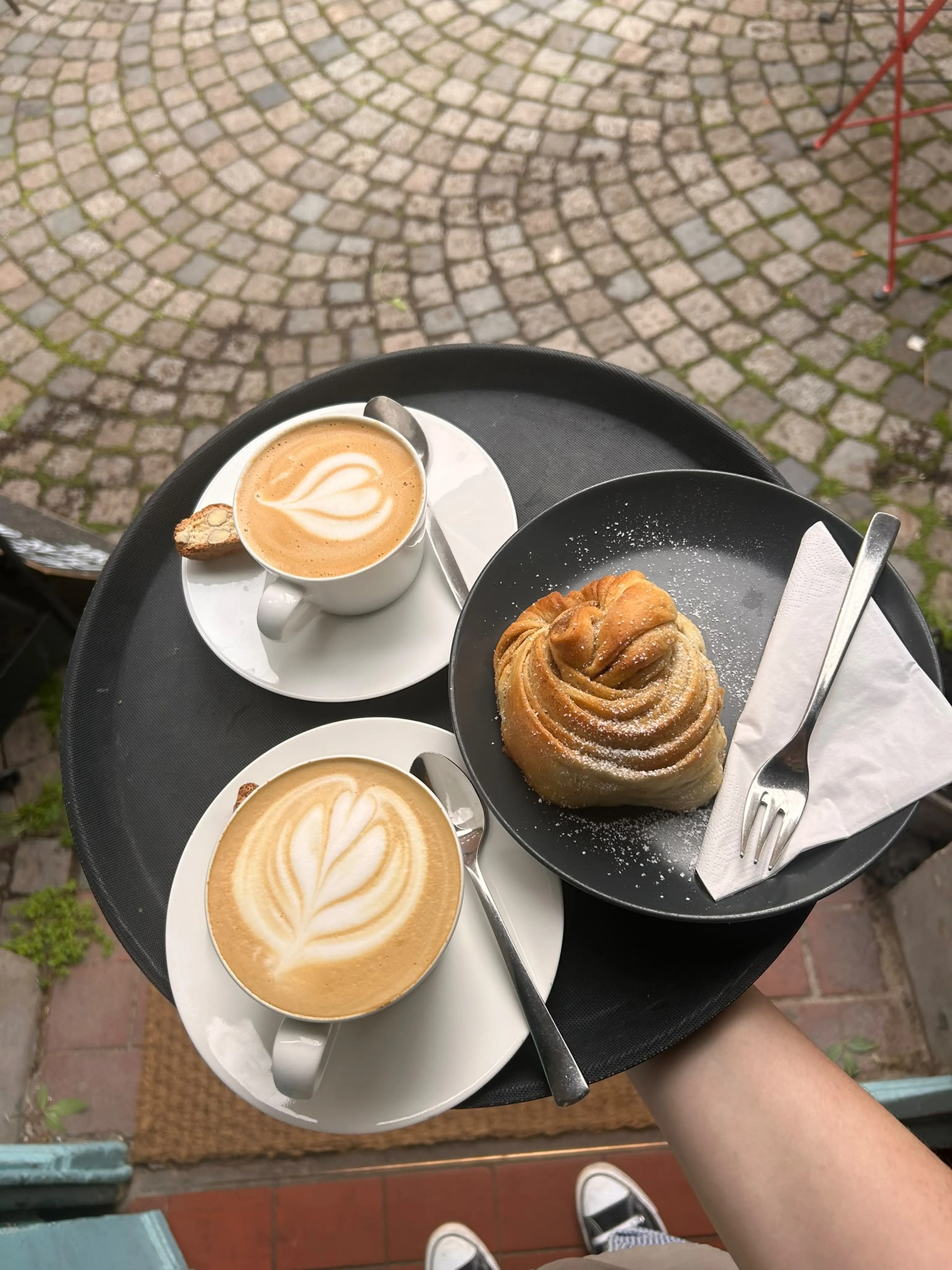 Cappuccino mit Latte Art und eine Zimtschnecke auf einem Tablett
