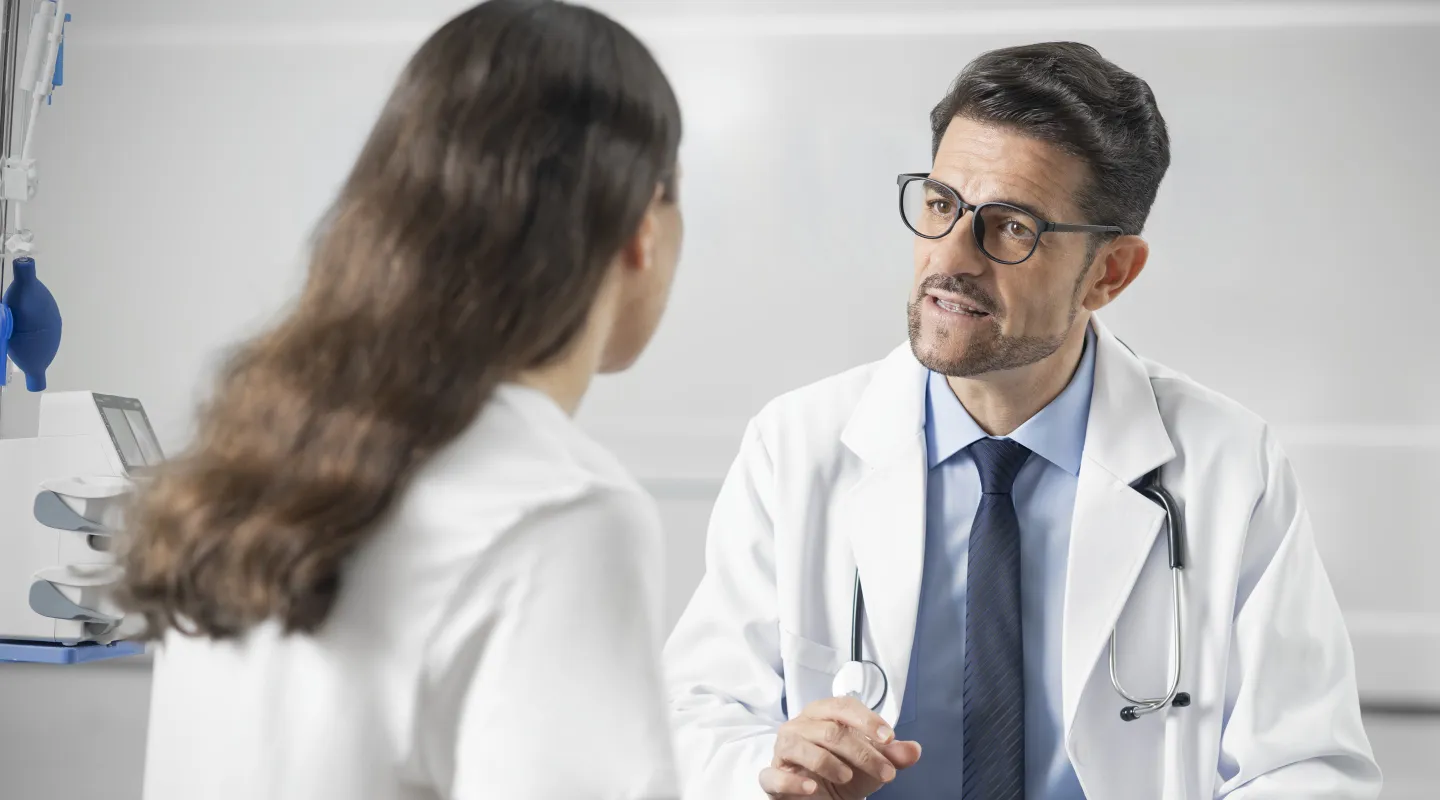 Clinician in a white coat talking with a colleague in a clinical room