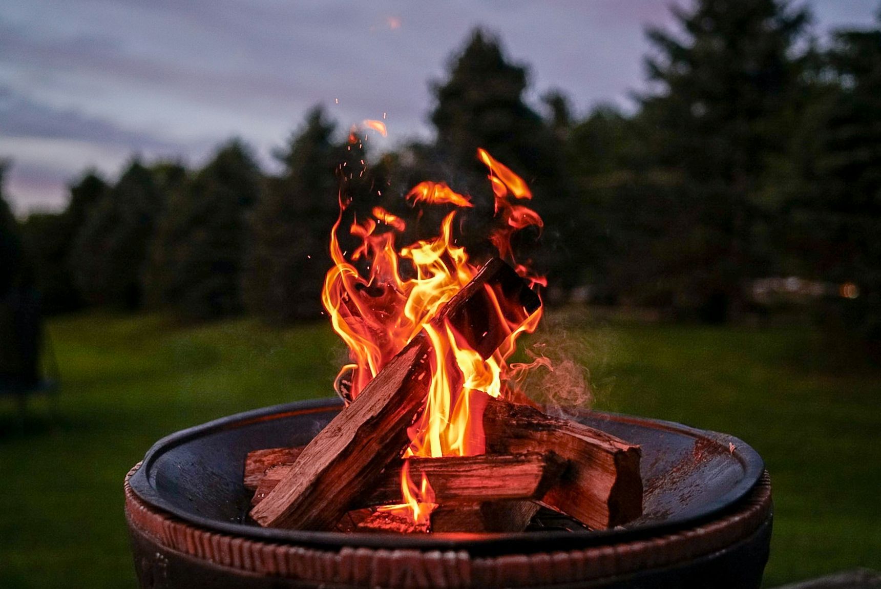 Vuurschaal met brandend hout in een tuin bij valavond