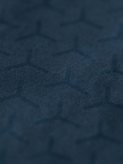 Close-up of a dark blue fabric with a subtle geometric pattern of interlocking, three-pronged shapes creating a textured appearance.