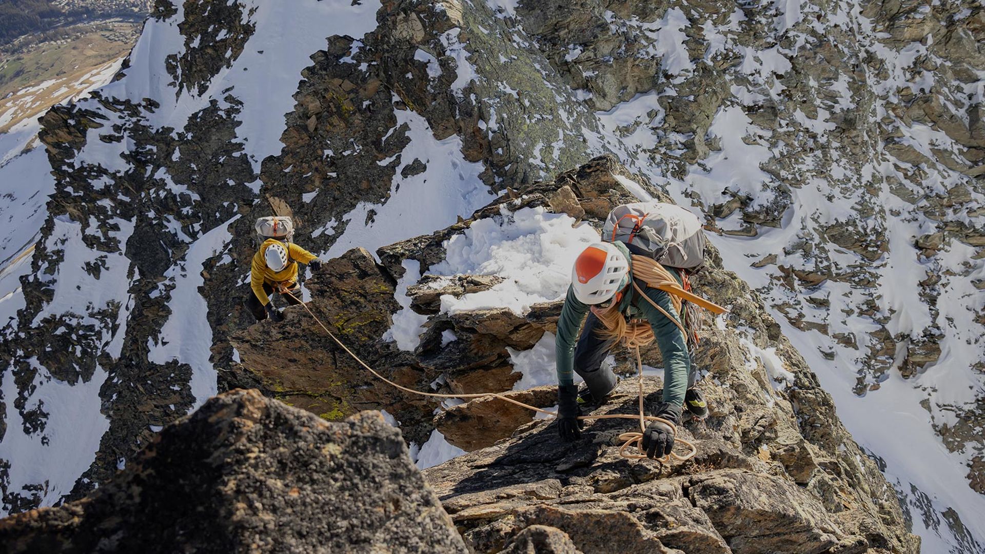 Two alpinists climbing a partially snowy mounitain.