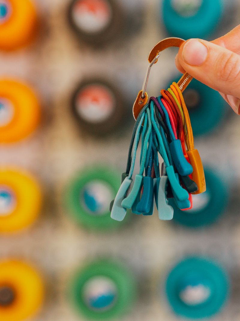 Hand holding a keyring with colorful zip replacements, blurred background of vibrant circular objects.