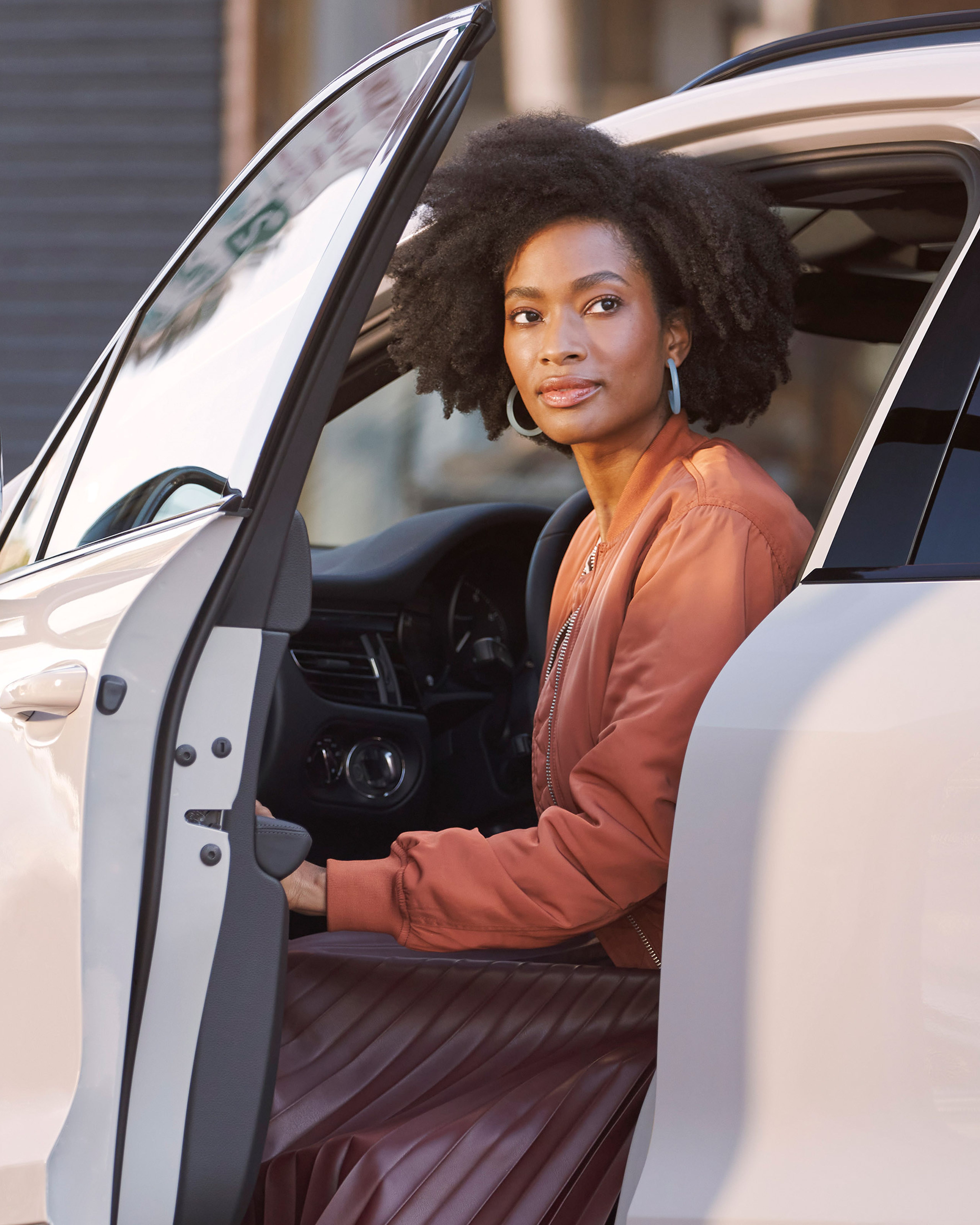 Woman seated in the driver’s seat of a white Porsche Macan with the door open.