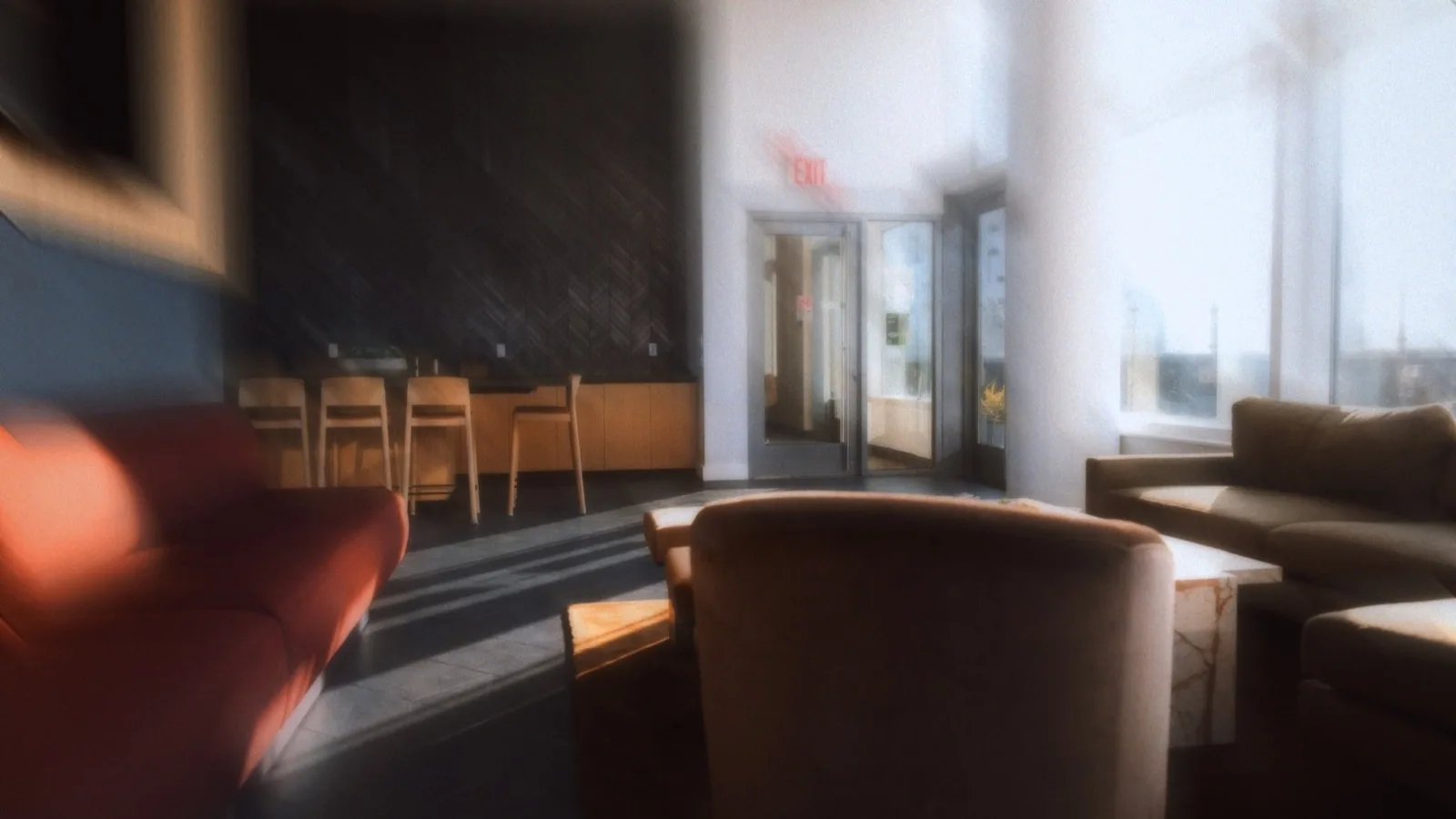 A sunlit apartment building lounge with armchairs, a sofa and a kitchen counter with stools