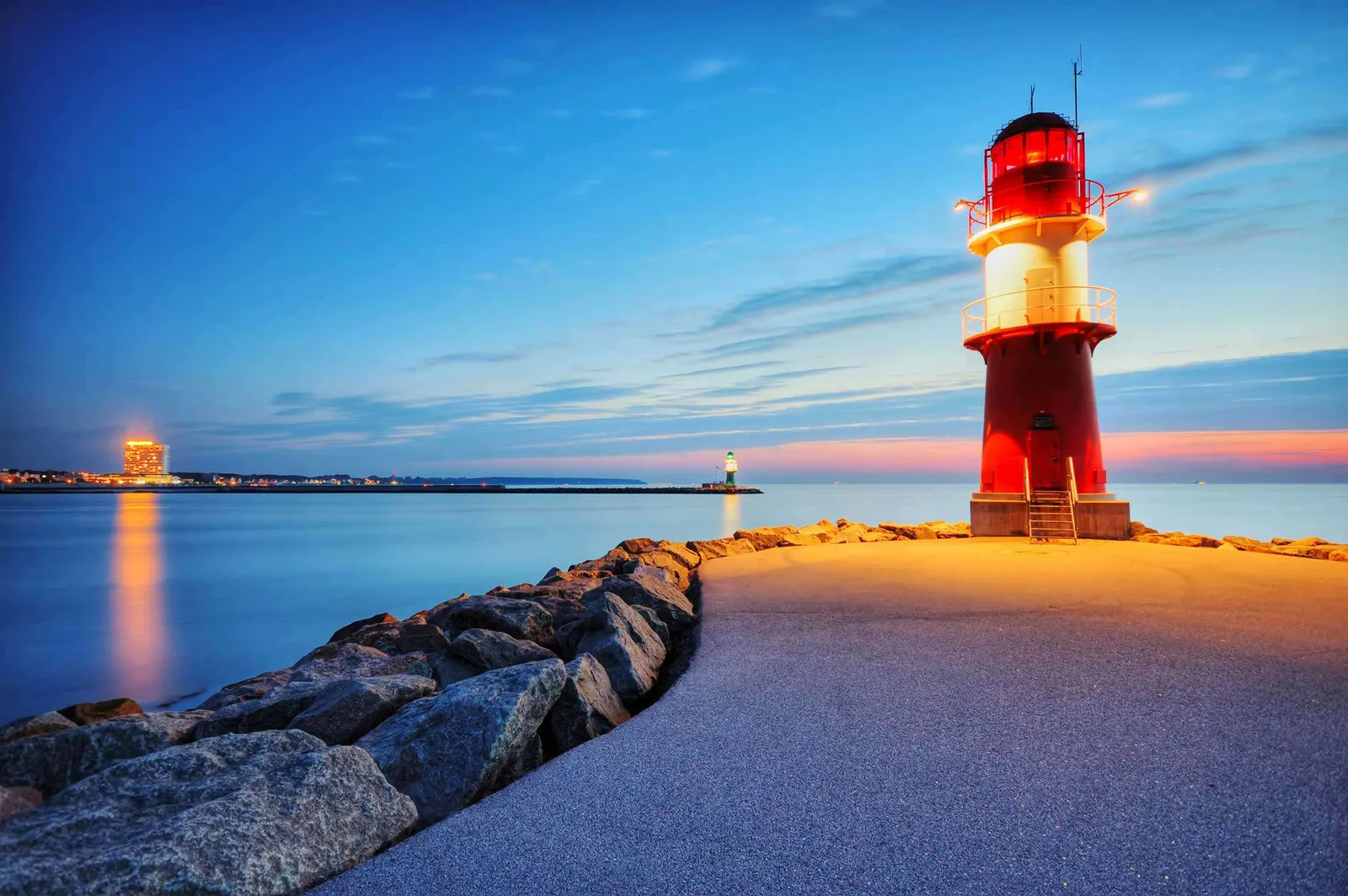 Der Warnemünder Leuchtturm bei Nacht, beleuchtet im Rahmen seines 25-jährigen Jubiläums, an der Küste von Rostock – www.the-green.de.