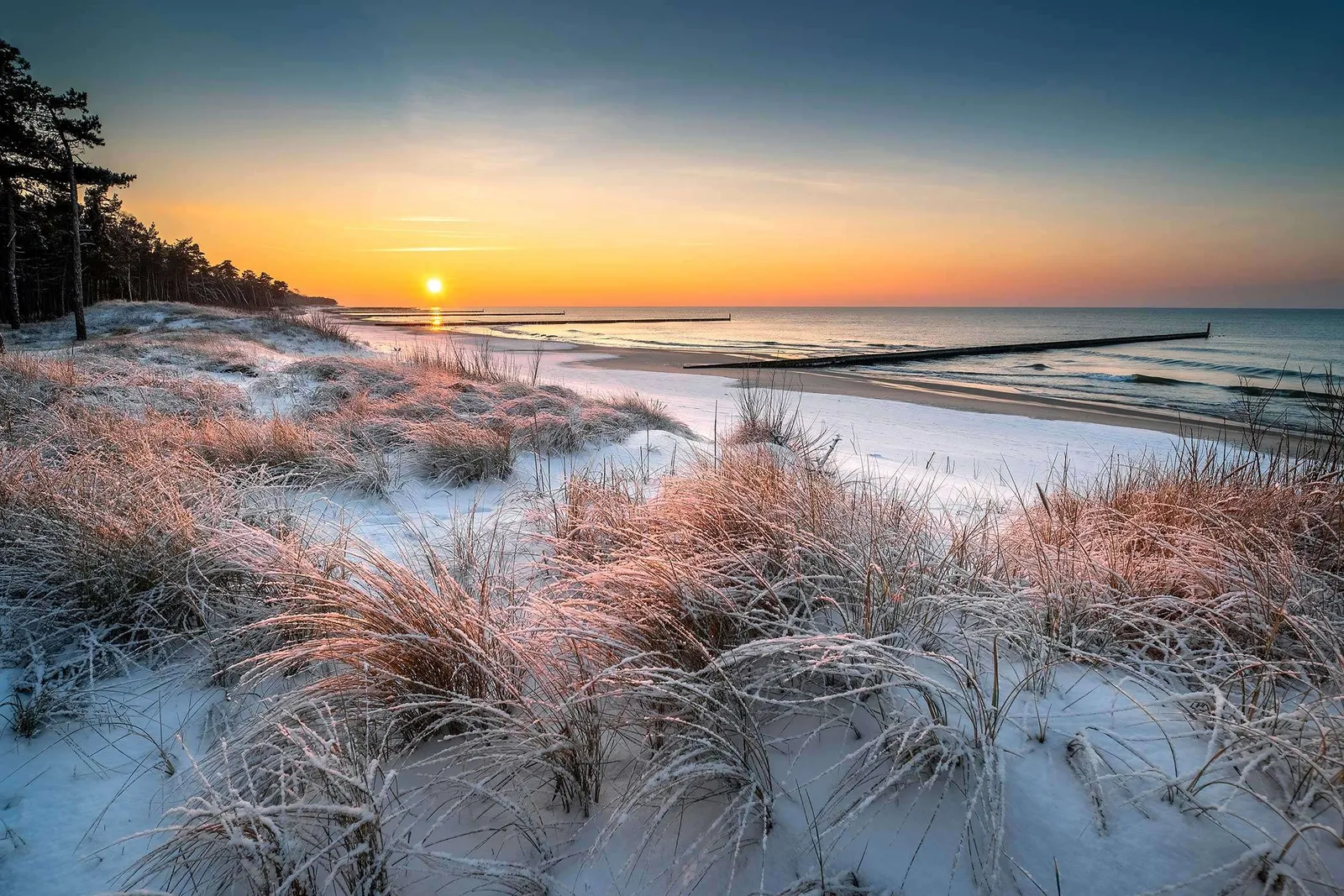 Winterliche Strandlandschaft in Rostock mit schneebedeckten Dünen und dem Meer im Hintergrund bei Sonnenuntergang – www.the-green.de