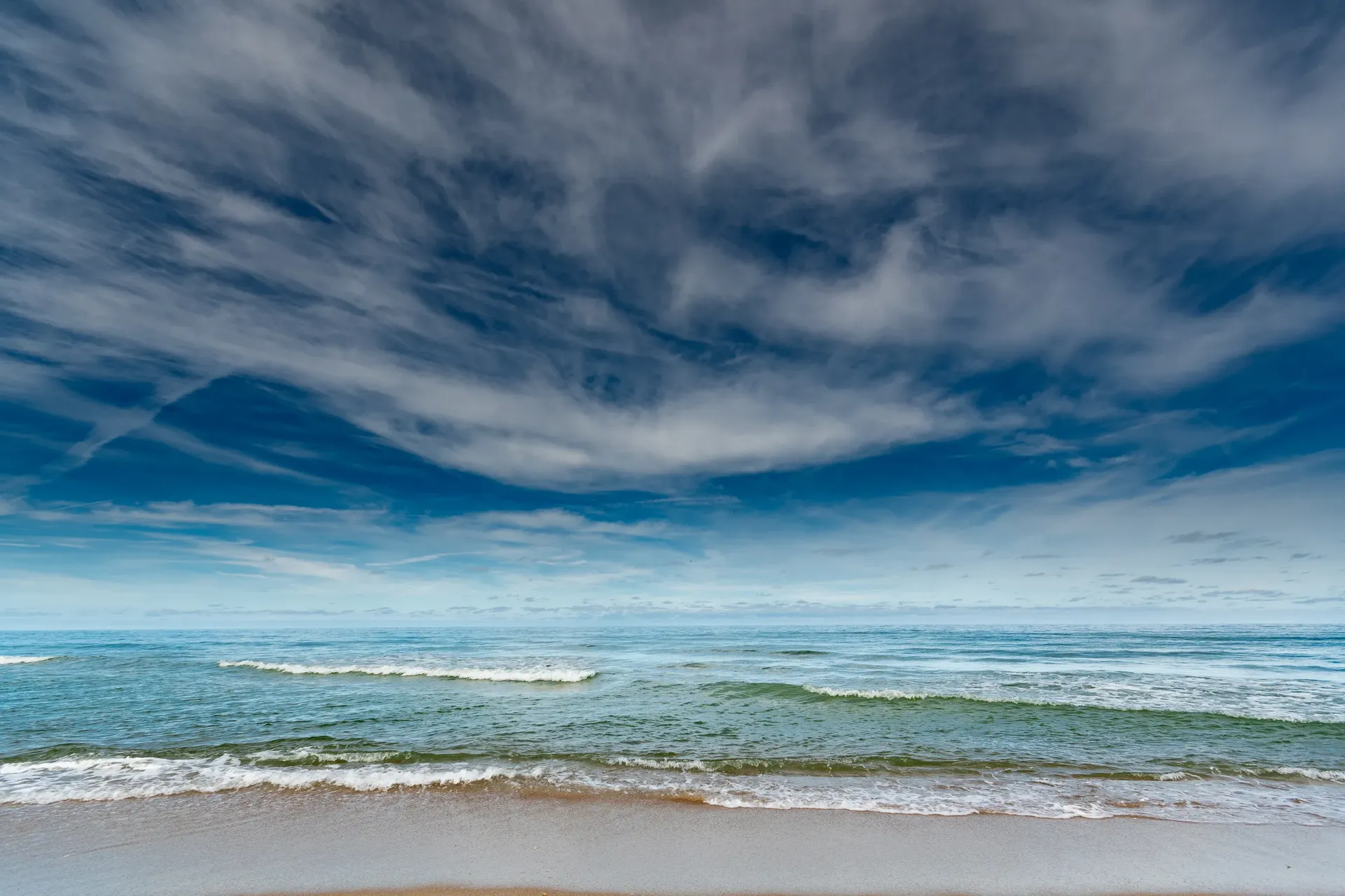 Wellen laufen an den Ostseestrand, darüber ein weiter Wolkenhimmel
