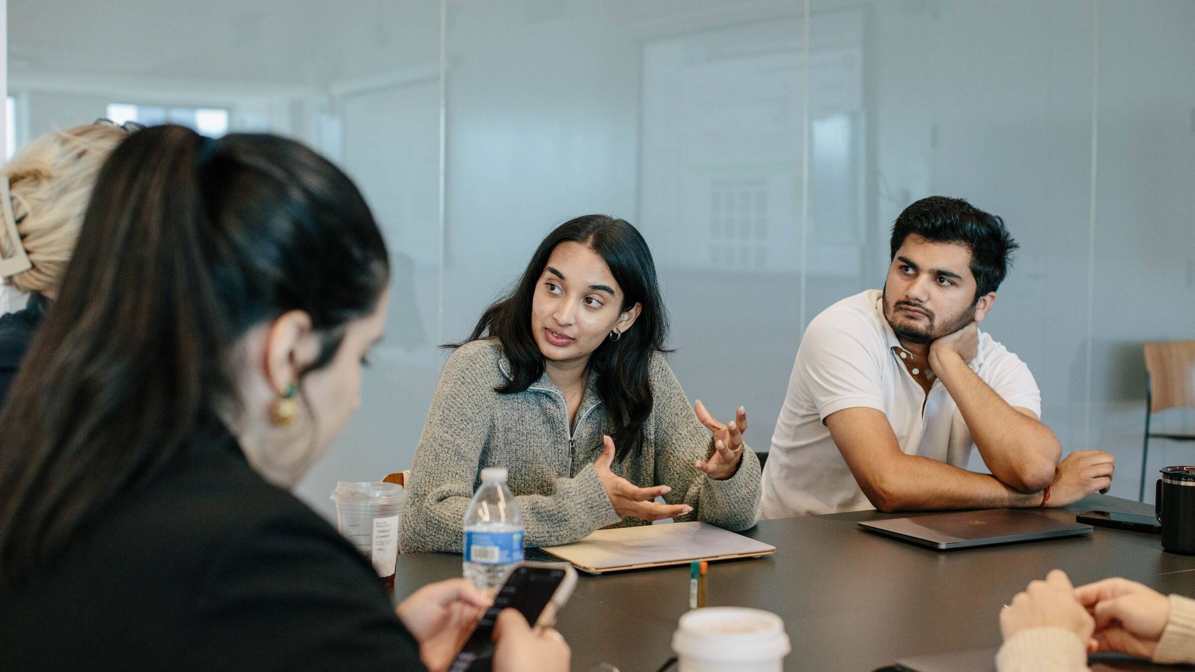 Two students in discussion at a table in a glass-walled meeting room