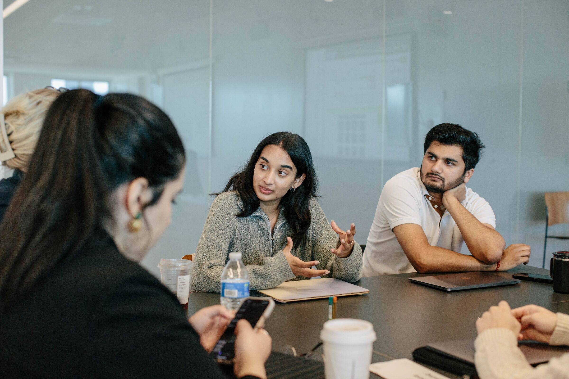 Two students in discussion at a table in a glass-walled meeting room