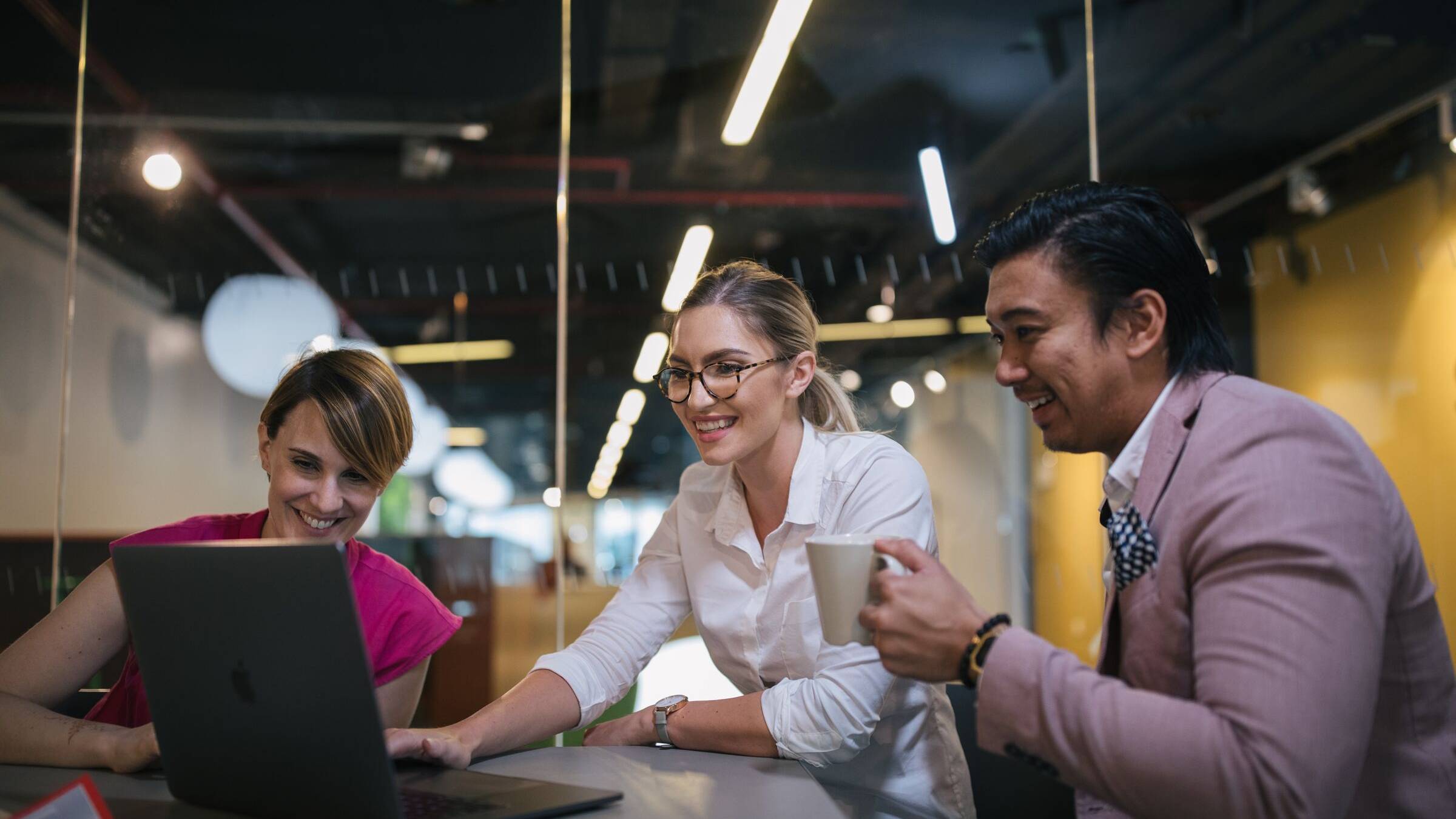 Three colleagues smiling and working together at a laptop in a modern office