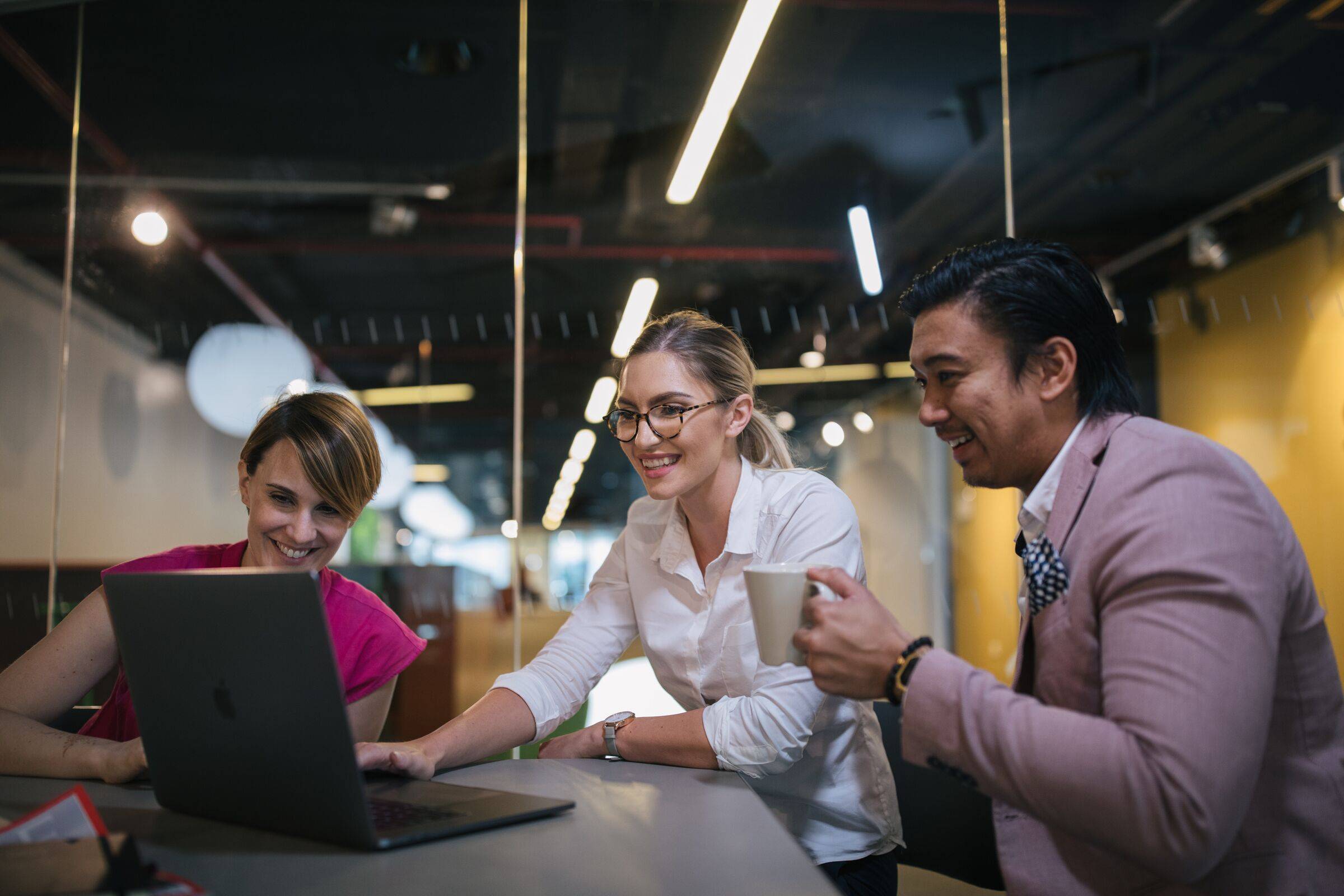 Three colleagues smiling and working together at a laptop in a modern office