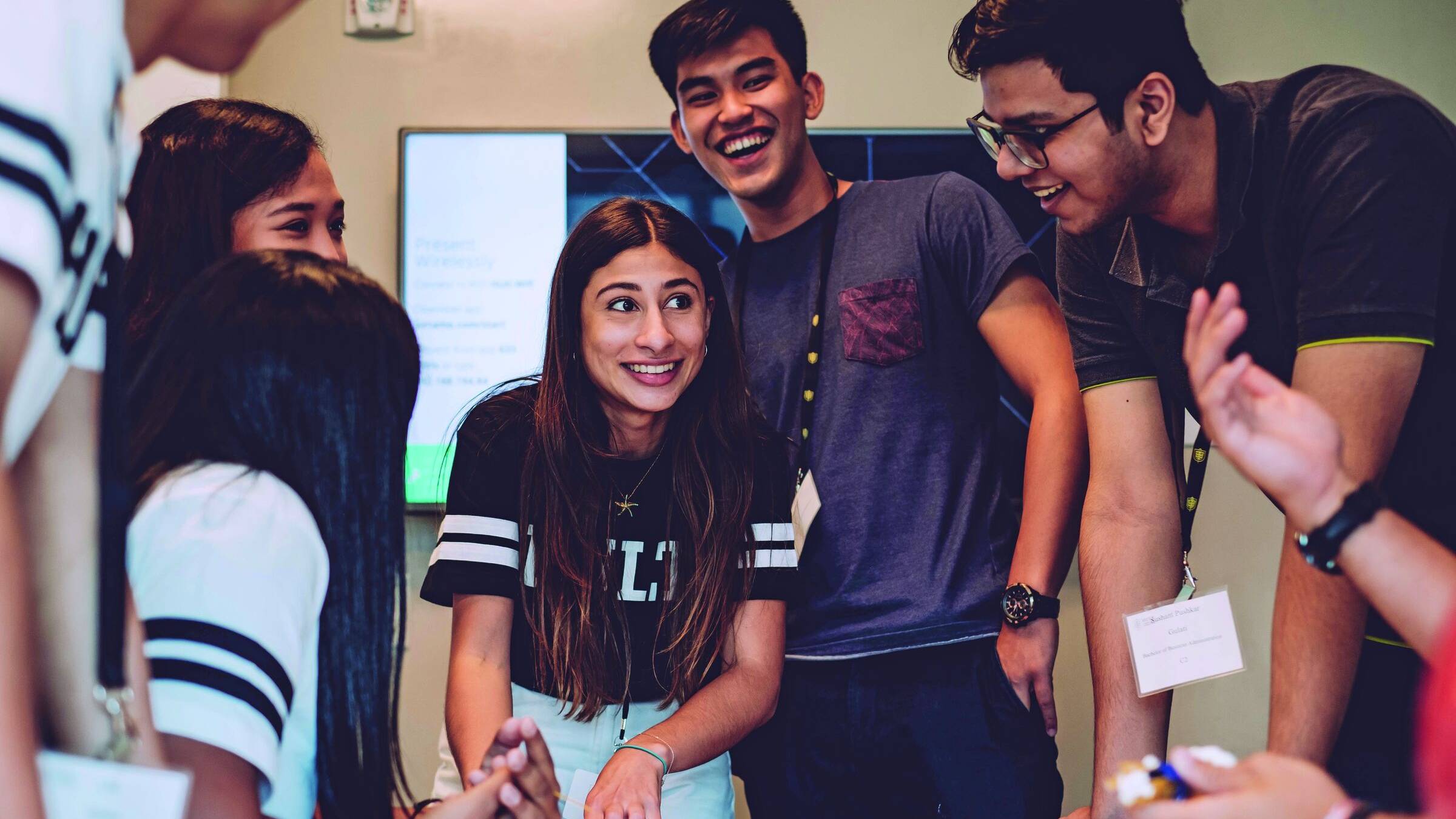 Group of smiling students leaning over a table, working on a project together