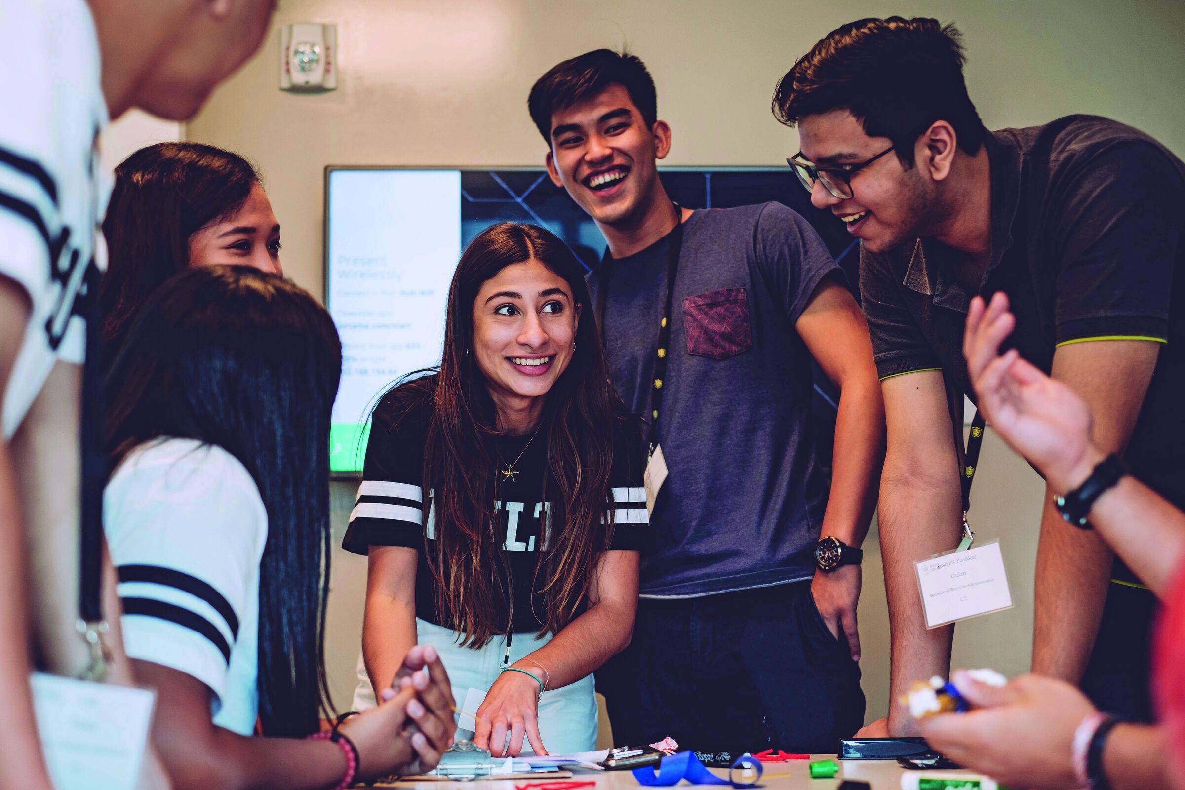 Group of smiling students leaning over a table, working on a project together