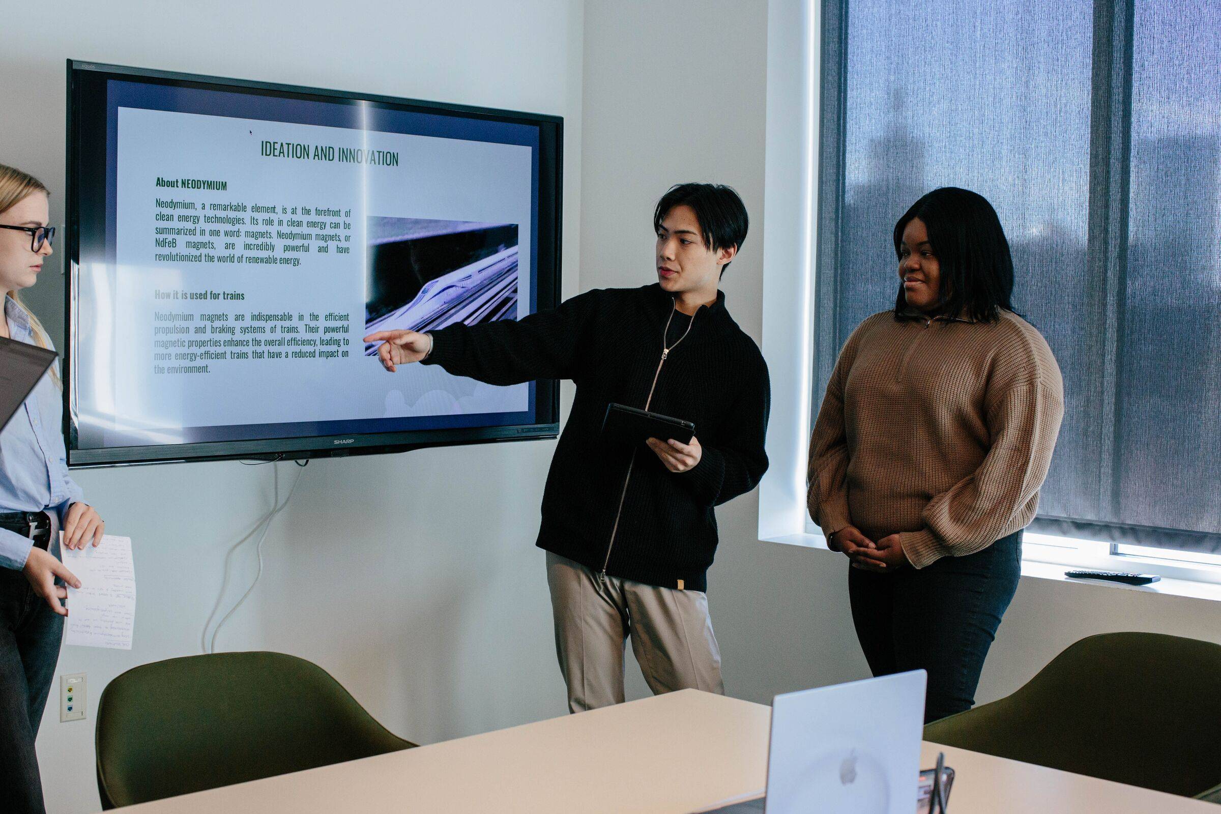 Two students presenting a slide on a wall-mounted screen in a meeting room