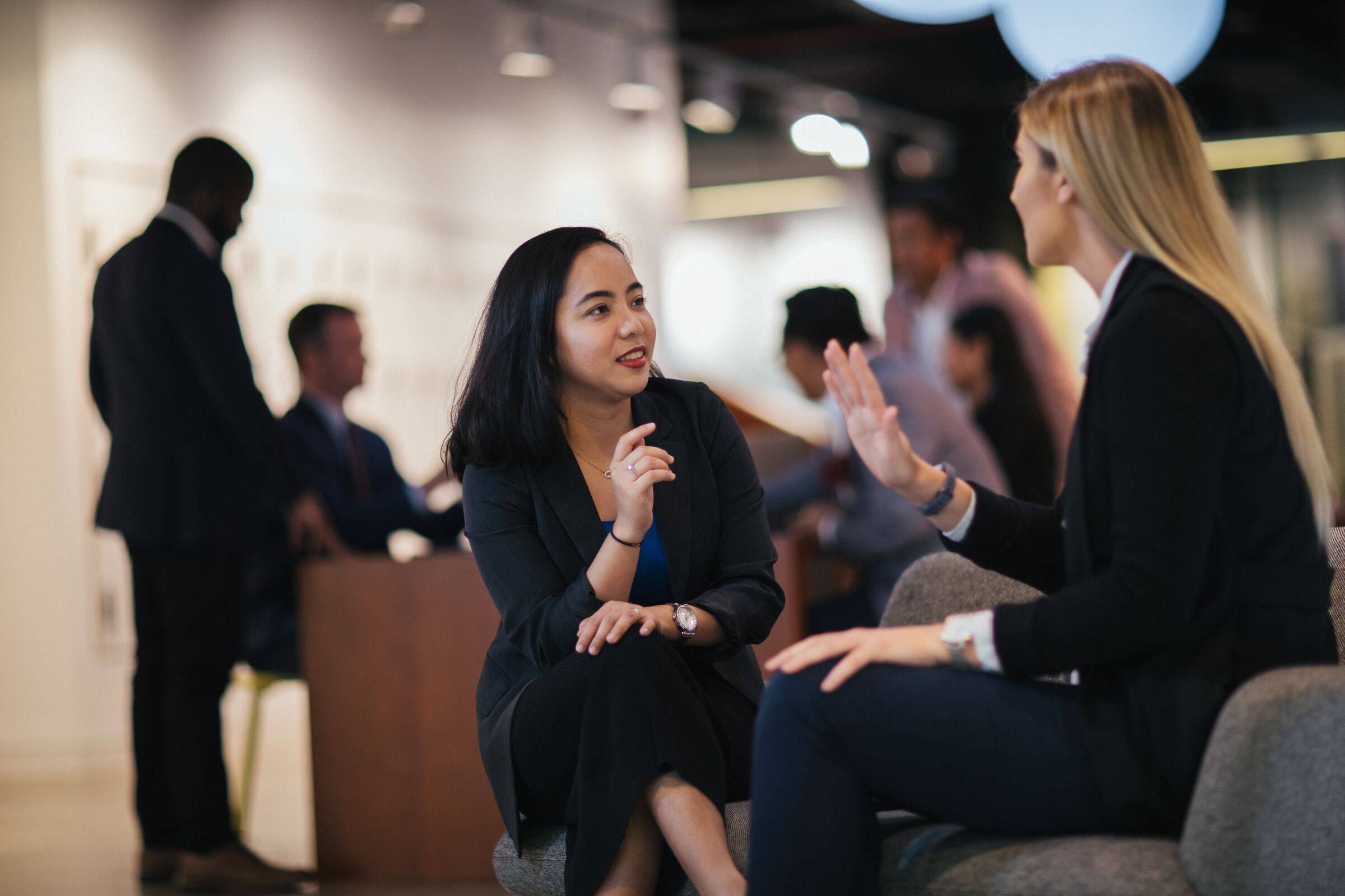 Two women in conversation at a networking event, with other guests in the background
