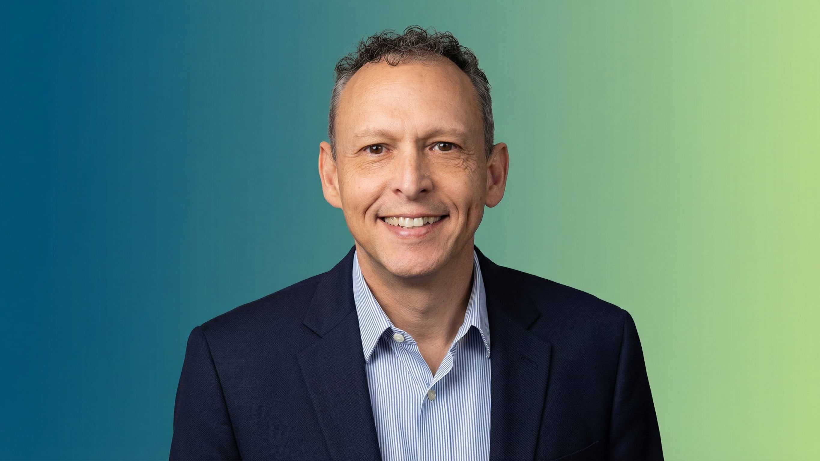 A man in a navy suit against a blue and green background