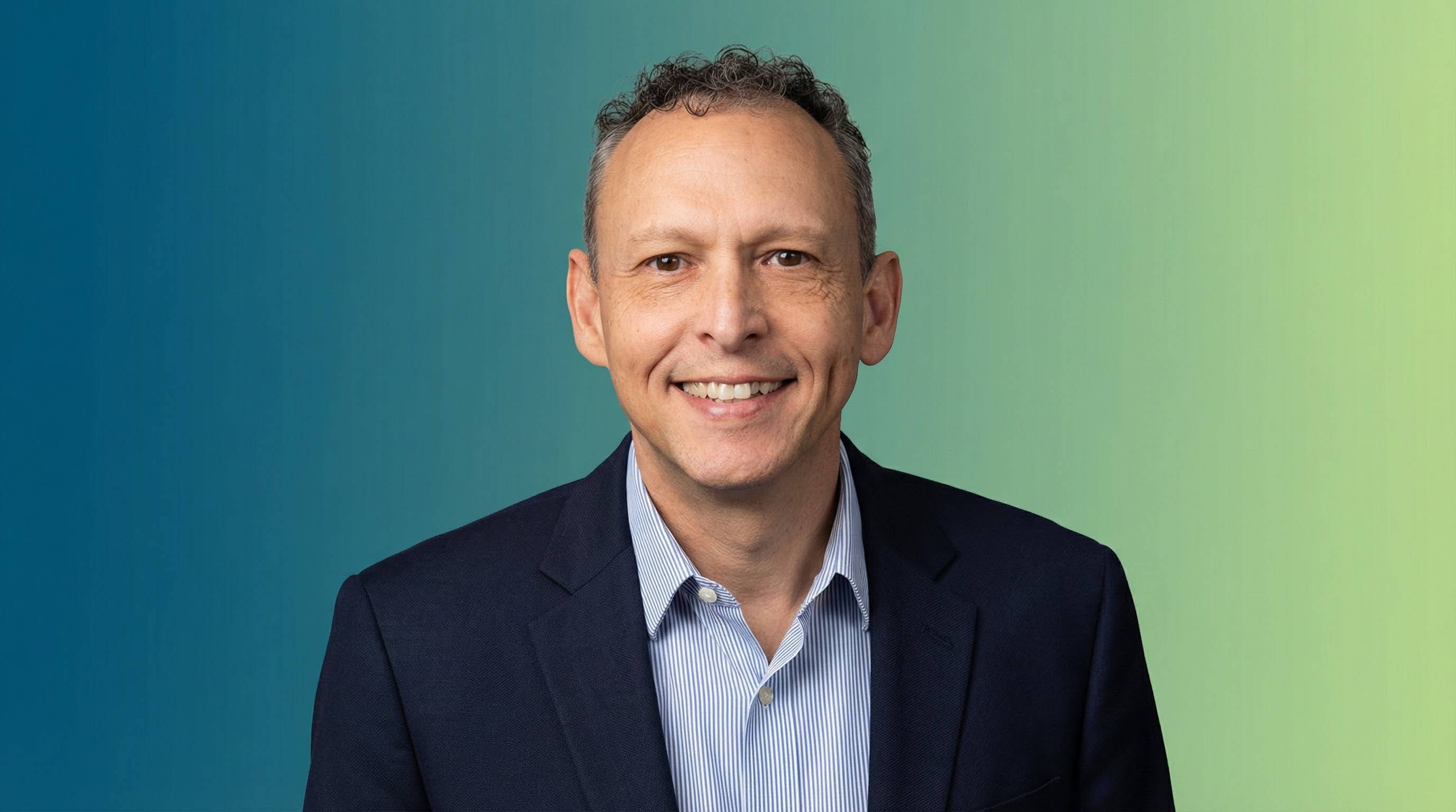 A man in a navy suit against a blue and green background