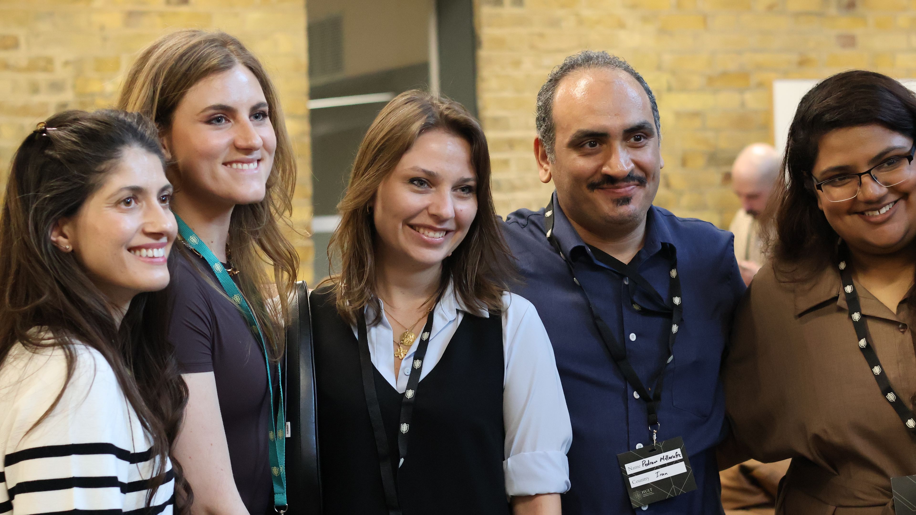 A group of five people, three women and two men, smiling and standing close together indoors, wearing badges and lanyards.