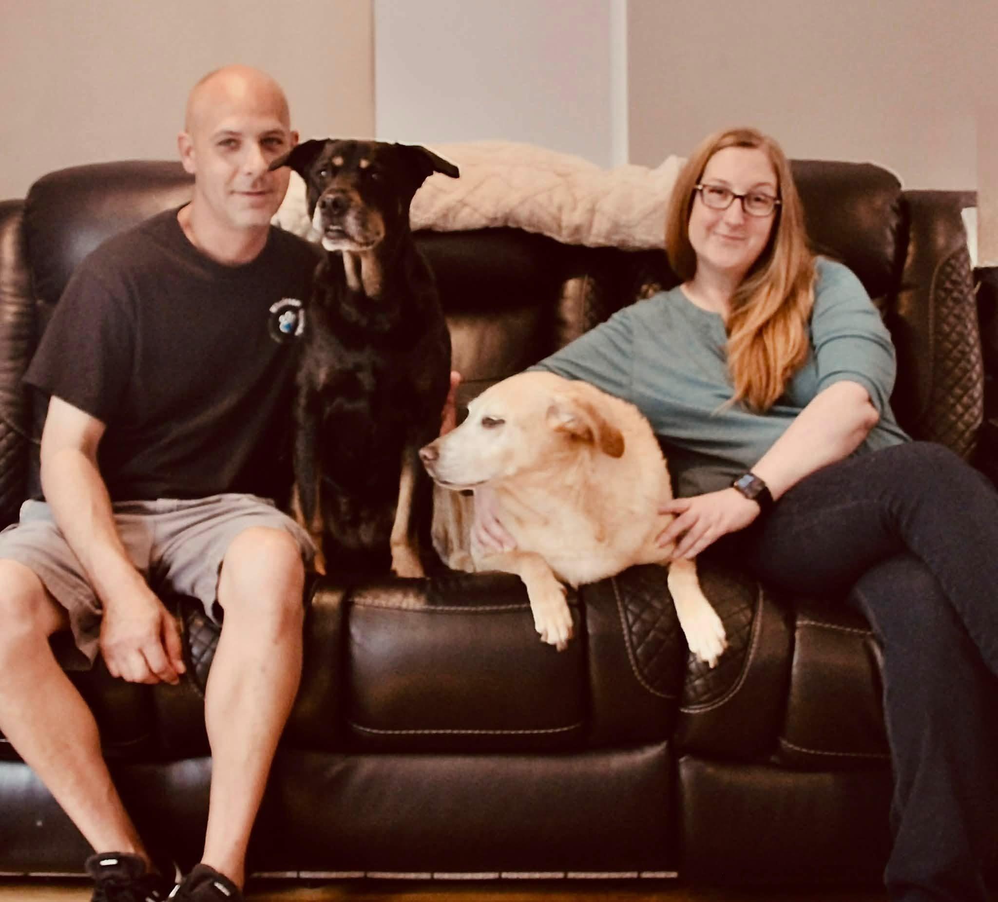 Cassandra and Eric on their couch at home with their dogs, Maya and Millie