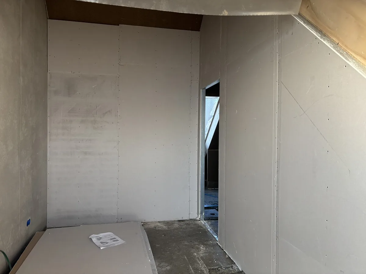 Een afgewerkte zolderwand met deurdoorgang, volledig dichtgezet met gipskartonplaten.