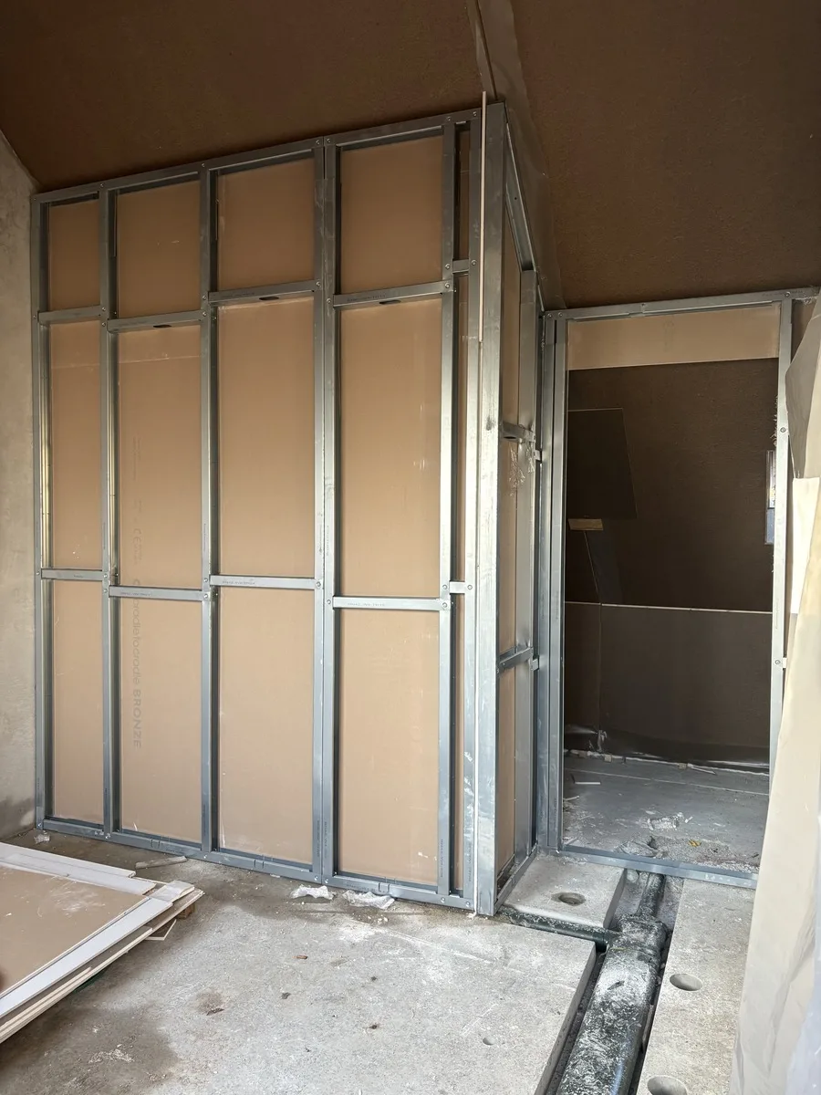 Het gemonteerde stalen frame van de zolderwand, met de gipskartonplaten er al achter en een doorgang naar de ruimte ernaast.