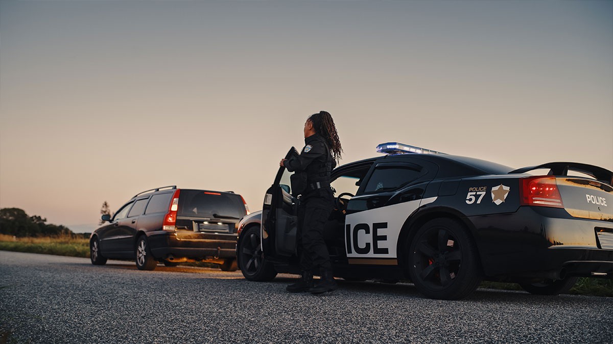 Police officer standing by patrol car after stopping a vehicle on a rural road at dusk.