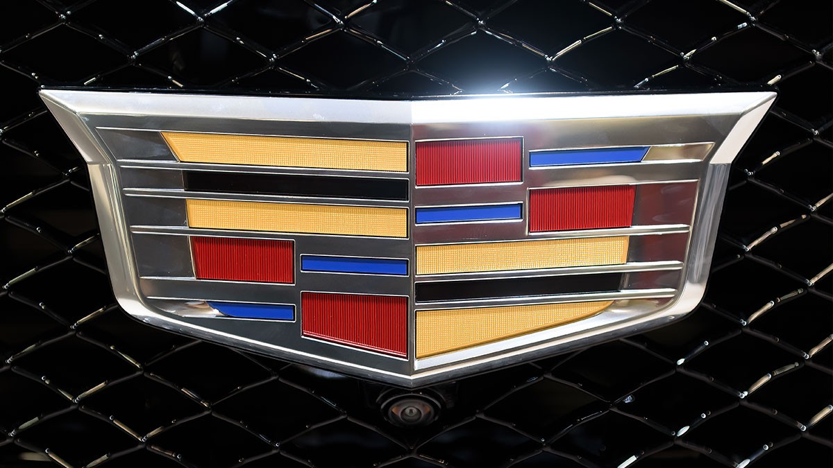 Close-up of a Cadillac logo on a black mesh grille, featuring a silver outline with red, blue, and gold accents.