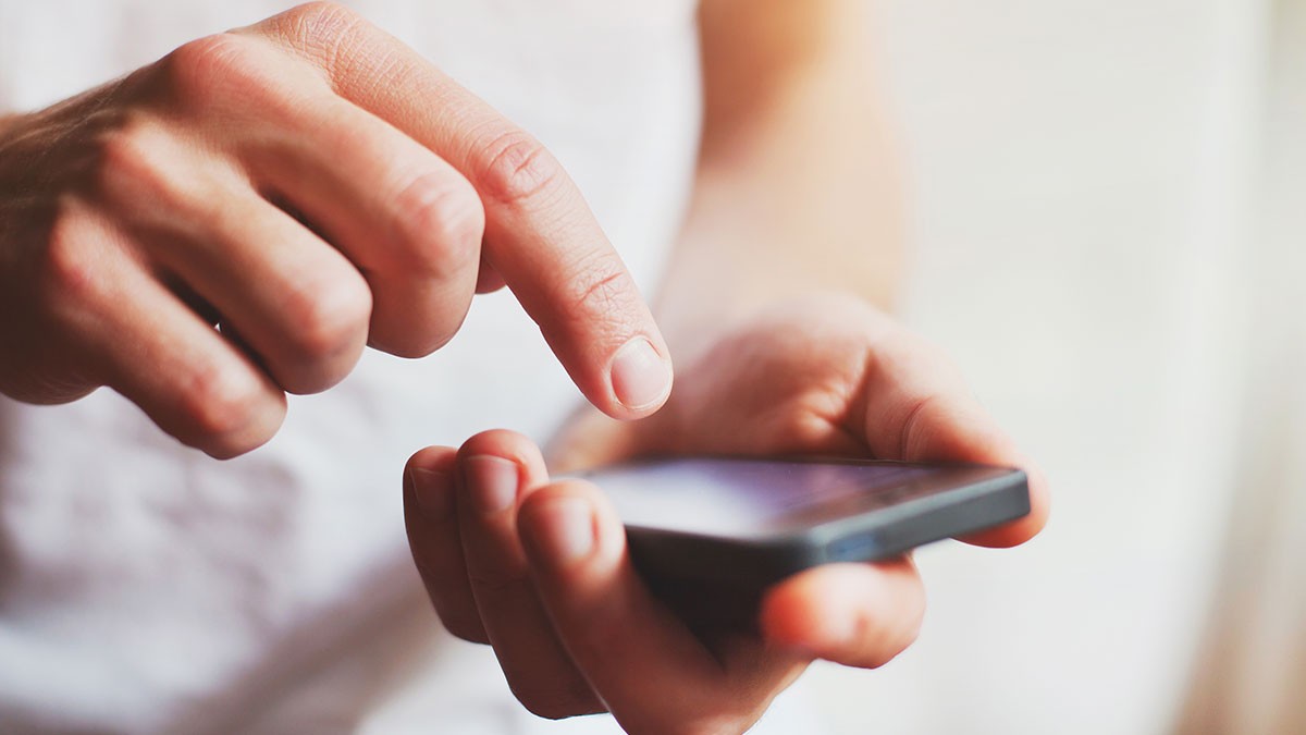 Close-up of a person using a smartphone, with one hand holding the device and the other hand tapping the screen.
