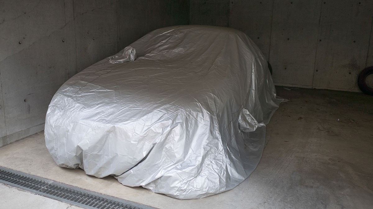 Car covered with a silver tarp in a dimly lit concrete garage.