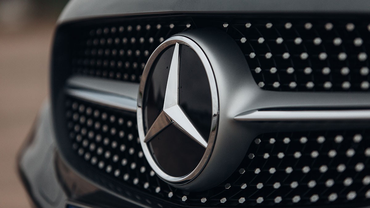 Close-up of a Mercedes-Benz logo on a car grille, featuring a metallic star emblem against a background of small circular patterns.