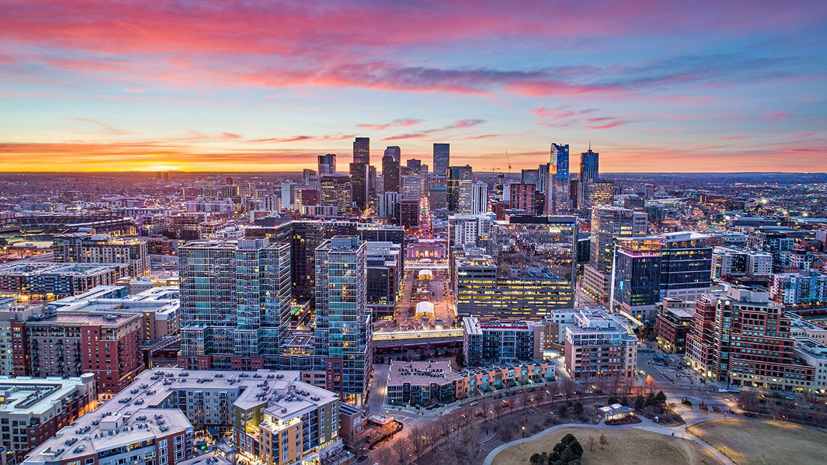 Aerial view of a city skyline at sunset, with colorful sky and modern buildings illuminated by city lights.