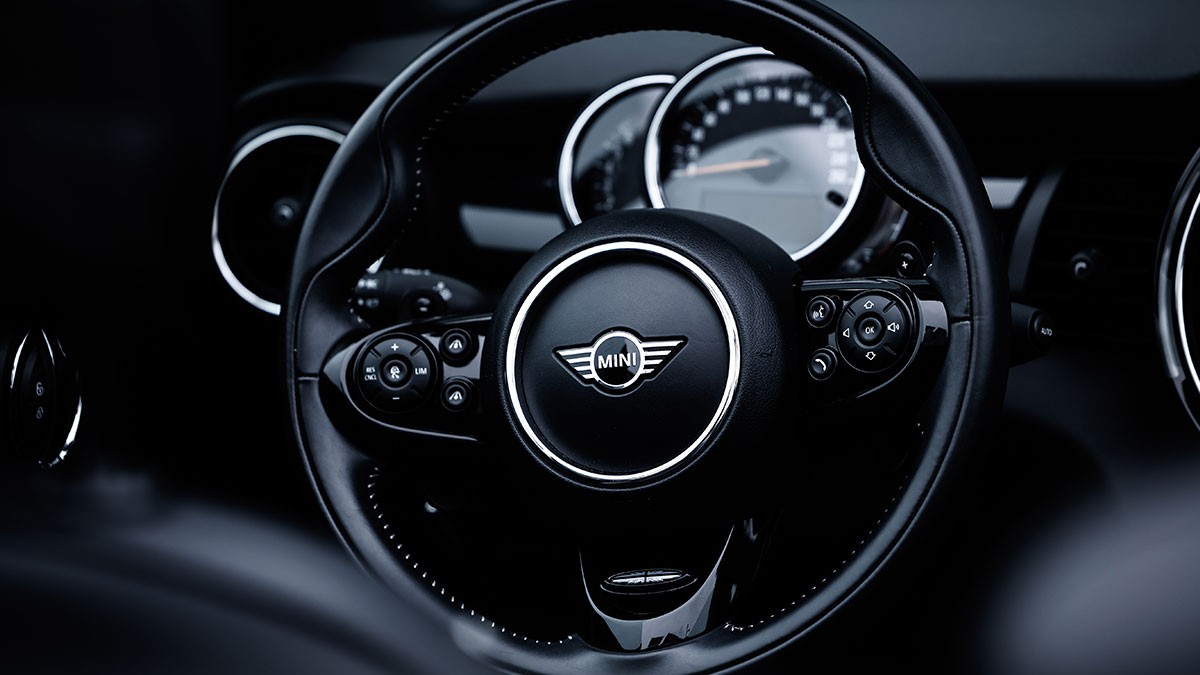 Close-up of a Mini car steering wheel, featuring the Mini logo in the center, with a speedometer visible in the background.