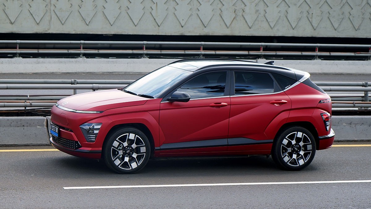 Red SUV with a black roof driving on a road, featuring modern design and alloy wheels, with a decorative wall in the background.