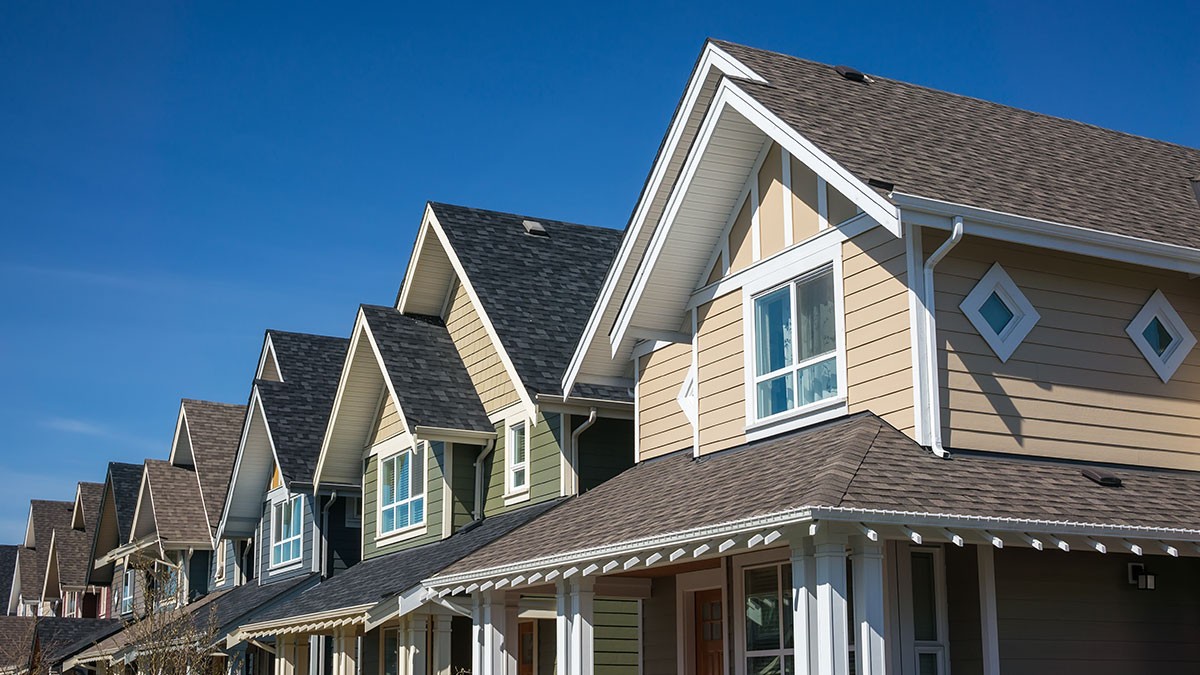 Row of modern suburban houses with sloped roofs against a clear blue sky.