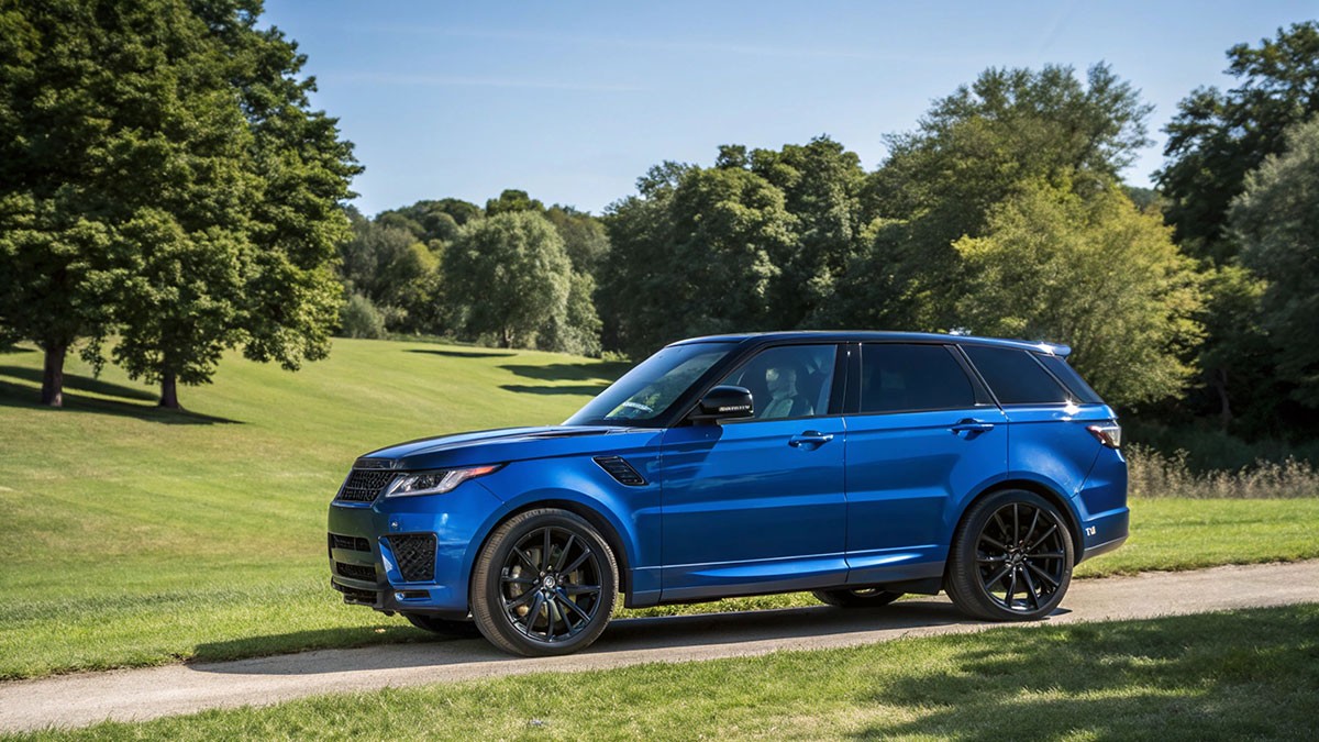 Blue luxury SUV with black wheels parked on a country lane beside green lawns and trees.