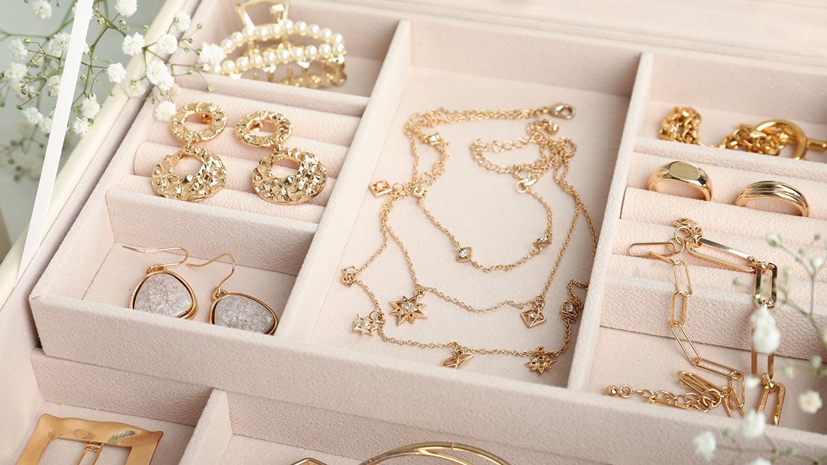 A jewelry box with various gold necklaces, earrings, and rings neatly arranged, surrounded by delicate white flowers.