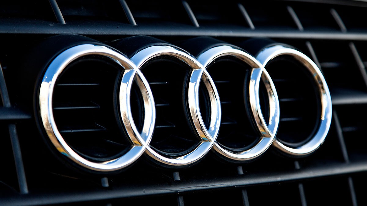 Close-up of the Audi logo, featuring four interlocking silver rings on a black grille background.