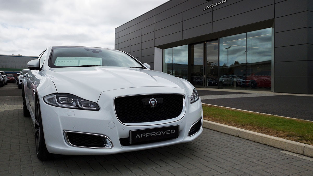 White Jaguar car parked in front of a modern dealership building under a cloudy sky.